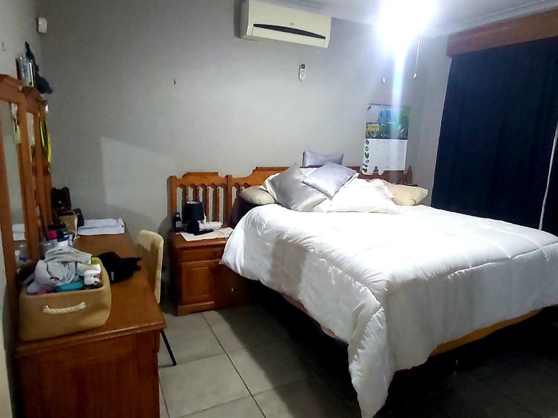 A bedroom featuring tiled flooring and a wall-mounted split-system air conditioner, with direct access to an adjoining en-suite bathroom.