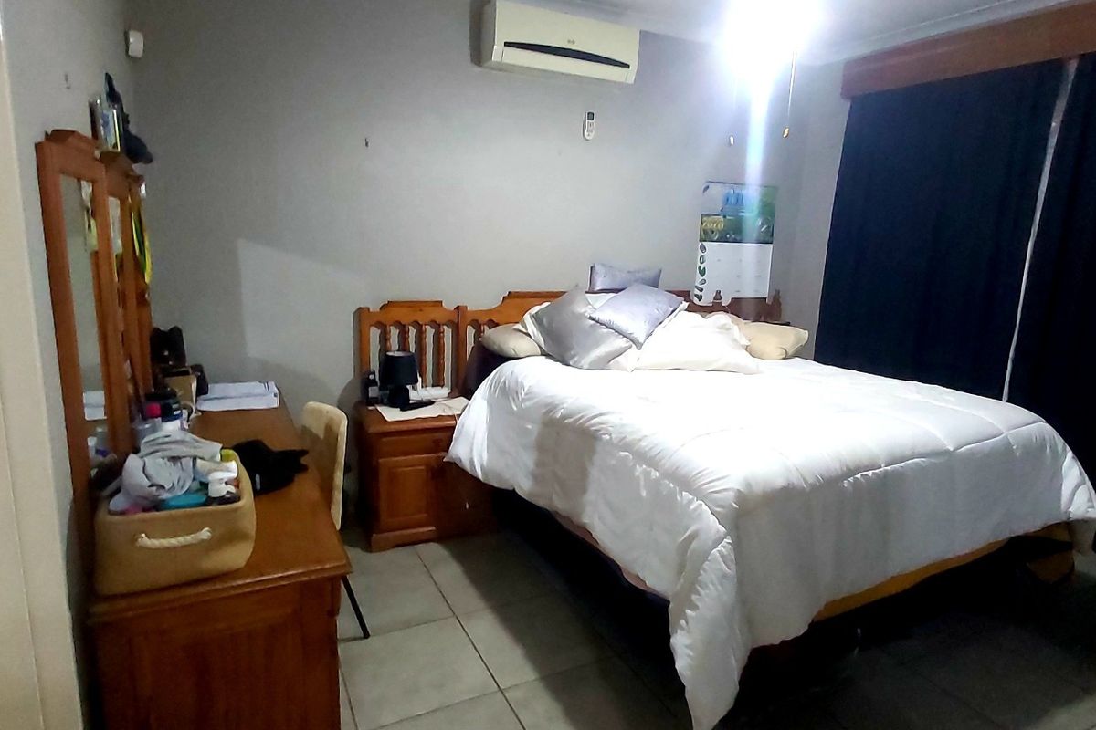 A bedroom featuring tiled flooring and a wall-mounted split-system air conditioner, with direct access to an adjoining en-suite bathroom.