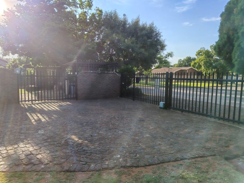 Front entrance area featuring a brick paved driveway, secure metal fencing, and a sliding gate providing access to the property.