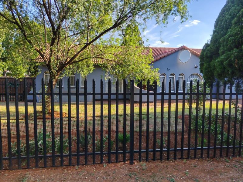 Front view of a residential house featuring a tiled roof, arched windows, and secure metal perimeter fencing.