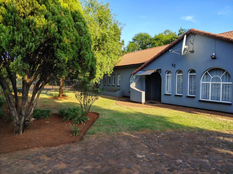 Front view of a single-story house featuring a paved driveway, arched windows with security bars, and a well-maintained garden area.