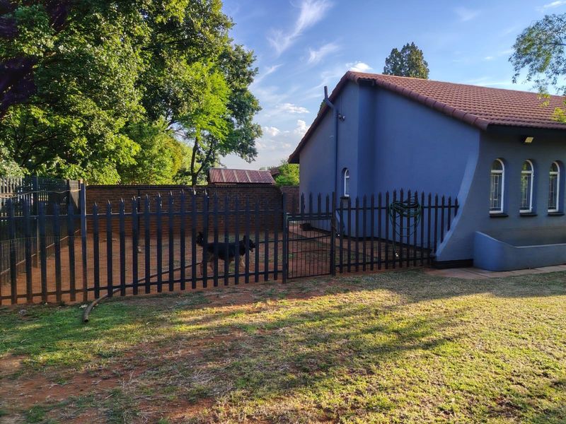 A view of the rear exterior of the house featuring blue painted walls, arched windows, a tiled roof, and secure metal palisade fencing.