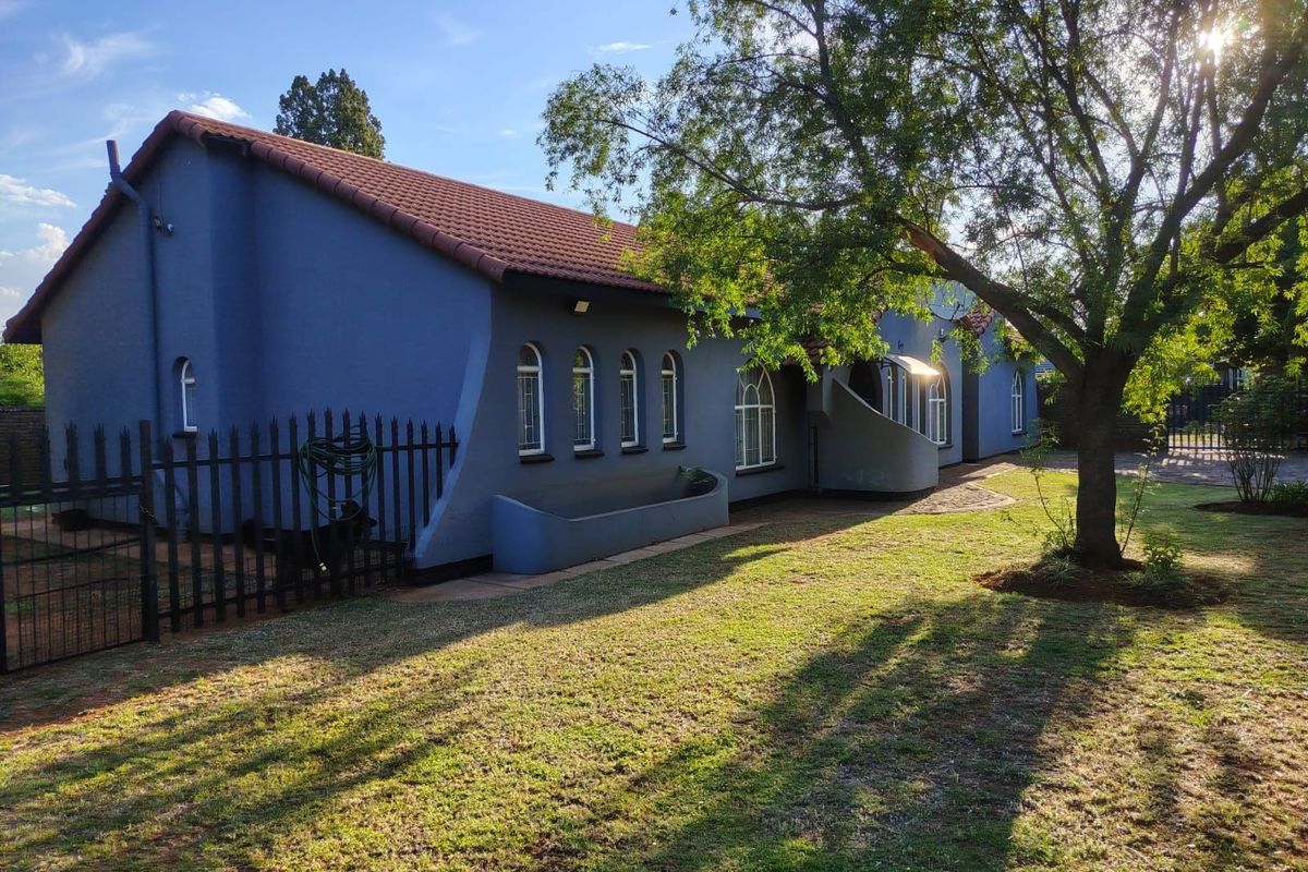 A view of the rear exterior of the house featuring a blue facade, arched windows, a tiled roof, and a well-maintained garden area.