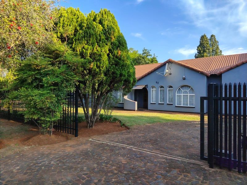 Front view of a single-story house featuring a cobblestone driveway, metal security fencing, and arched windows under a tiled roof.