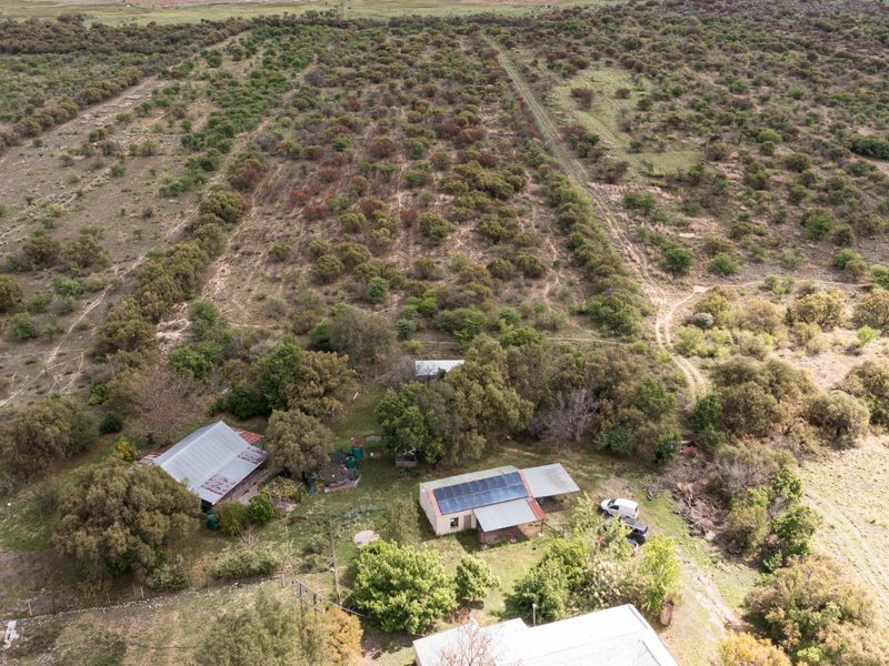 Aerial view of a small holding property featuring multiple structures with metal roofing, solar panel installations, and expansive surrounding natural landscape.