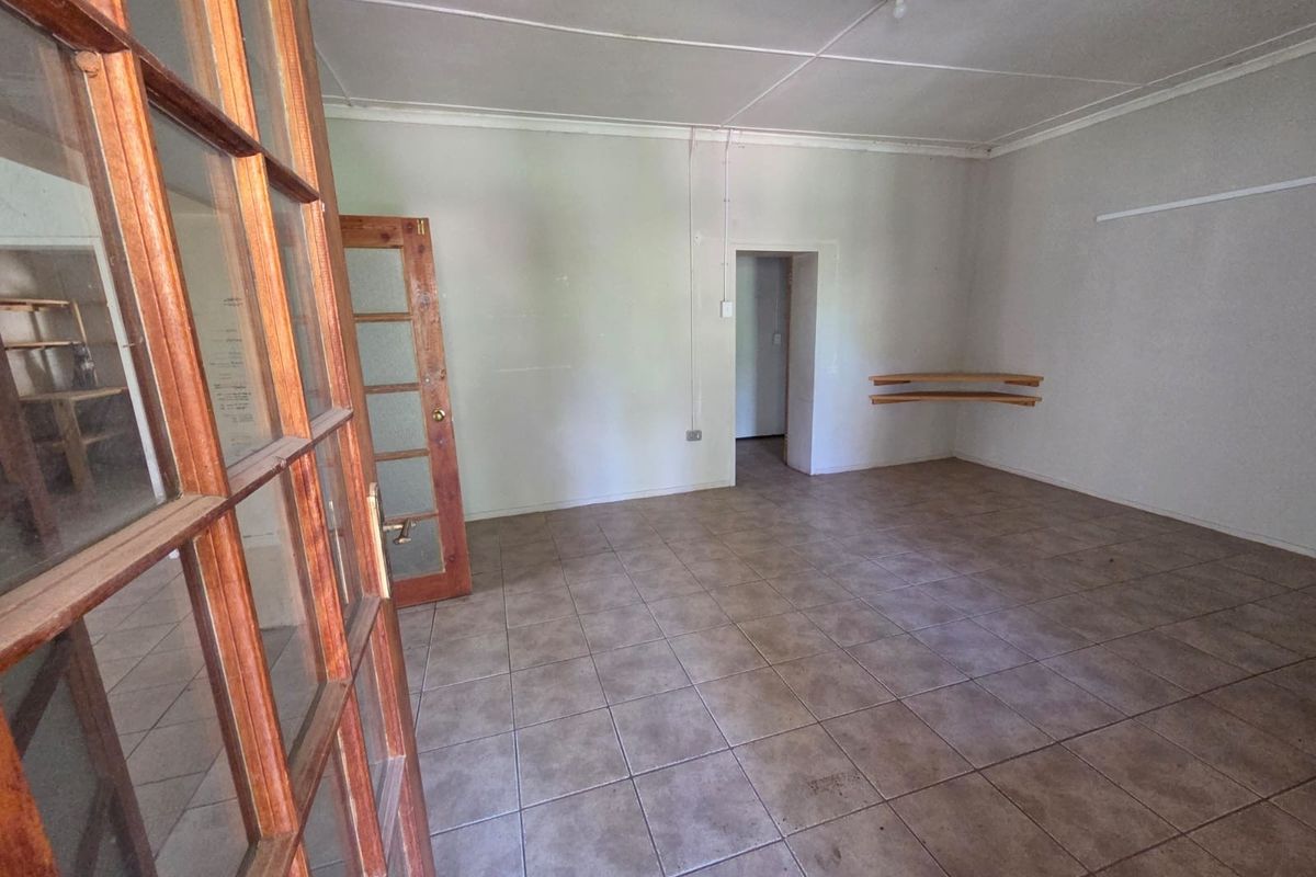 An empty living area featuring tiled flooring, a wooden framed glass door, and built-in corner shelving, offering a blank canvas for interior design.