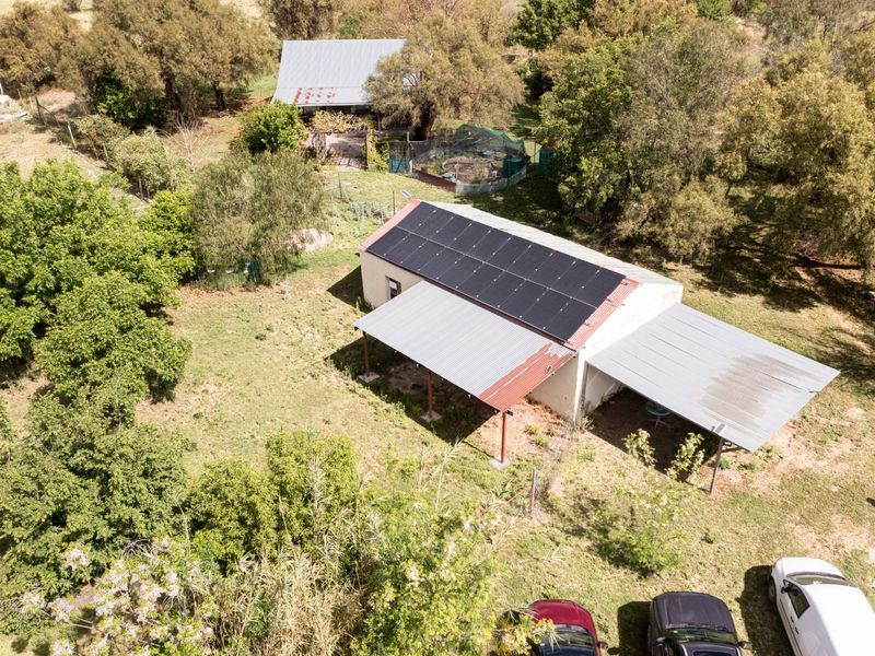 Aerial view of a small holding property featuring a main dwelling with solar panels, a covered patio, carport, and surrounding garden area.