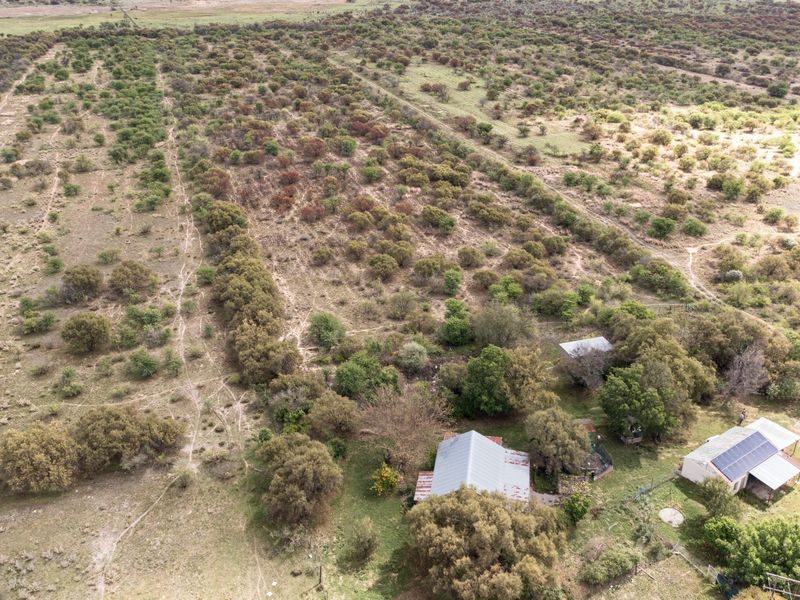 Aerial view of a small holding property featuring multiple structures with corrugated metal roofing, solar panels, and expansive surrounding natural landscape.