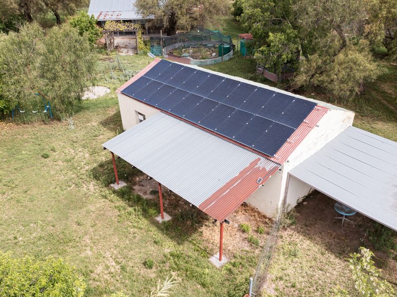 Aerial view of a small holding structure featuring a large solar panel array and a corrugated metal roof with visible signs of weathering.