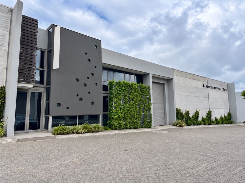 Modern industrial facade featuring a paved driveway, roller shutter door, and a striking vertical garden wall with contemporary architectural detailing.