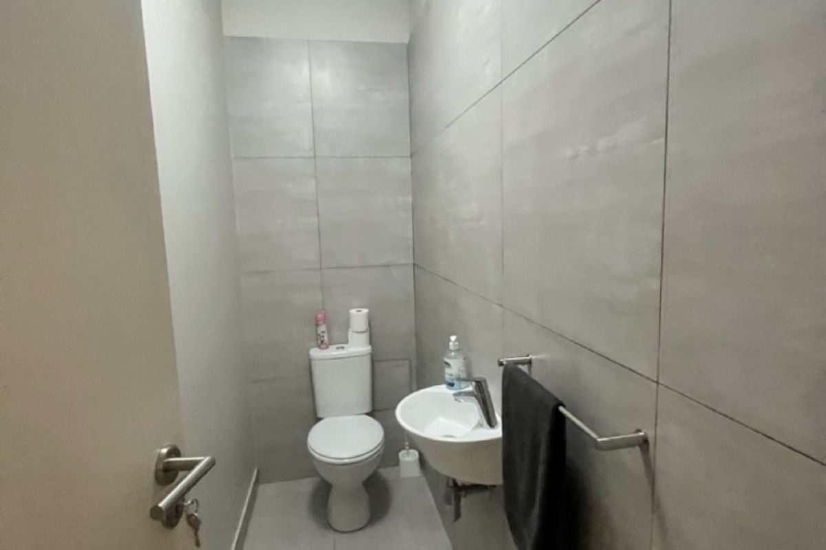 A compact, modern industrial-style bathroom featuring neutral ceramic wall and floor tiles, a wall-mounted basin, and a standard toilet.