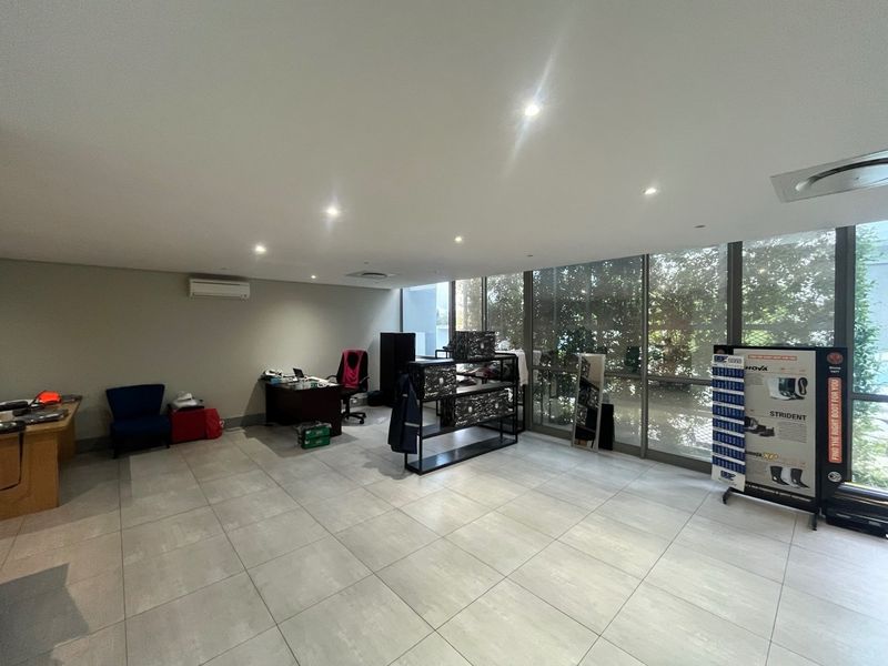 A spacious, well-lit office area featuring large floor-to-ceiling windows, modern tiled flooring, and a wall-mounted air conditioning unit.