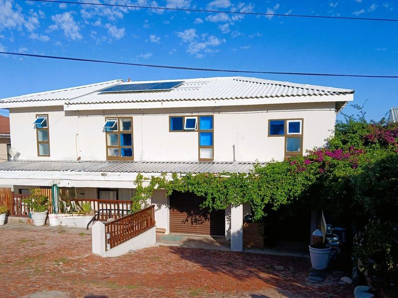 Front elevation of a two-story house featuring a corrugated metal roof with solar panels, a brick driveway, and a ground-level garage.