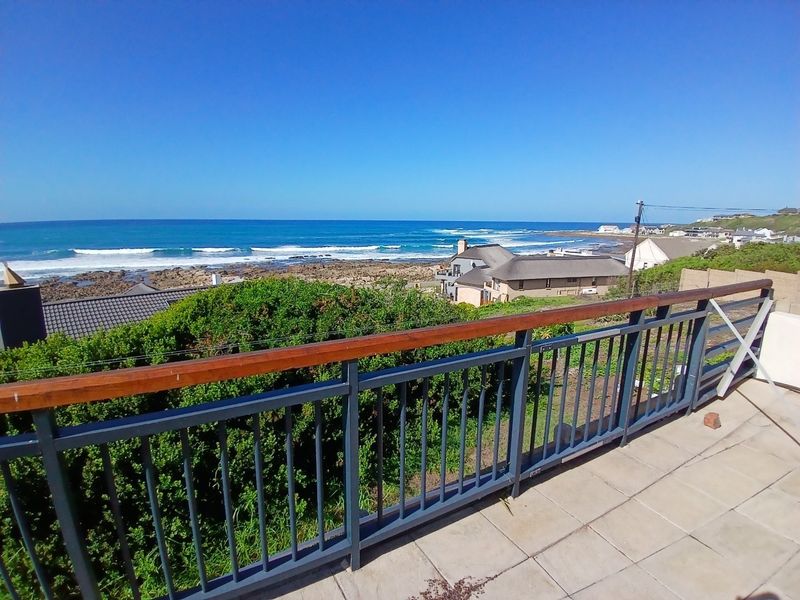 Elevated balcony view overlooking the coastline, featuring a metal railing with a wooden handrail and tiled flooring.