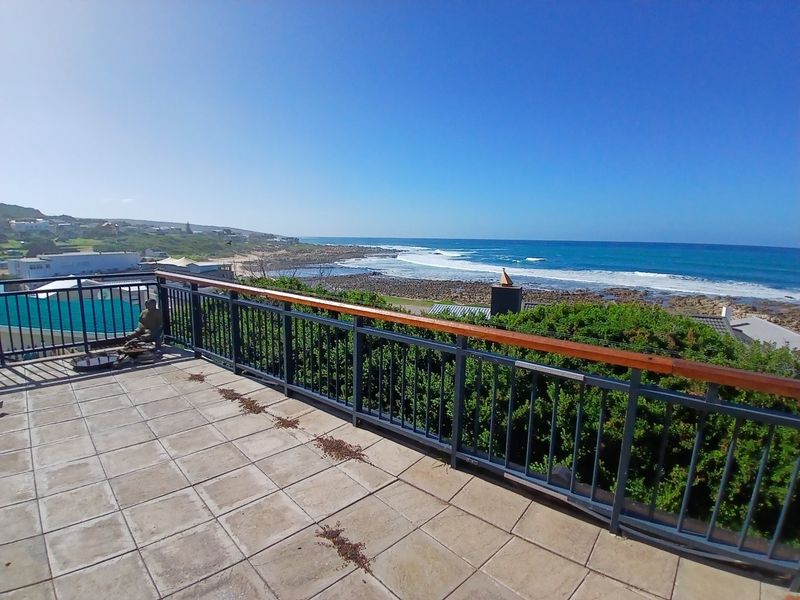 Spacious outdoor balcony featuring tiled flooring and a metal balustrade with a wooden handrail, offering expansive coastal and ocean views.
