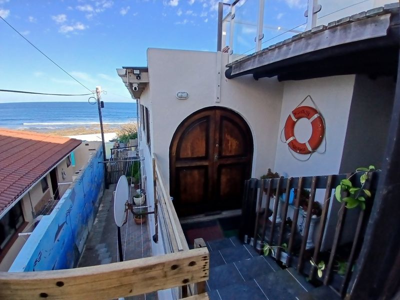 Rear exterior view featuring an arched wooden entrance door, tiled staircase, and glass balustrade with a coastal outlook.