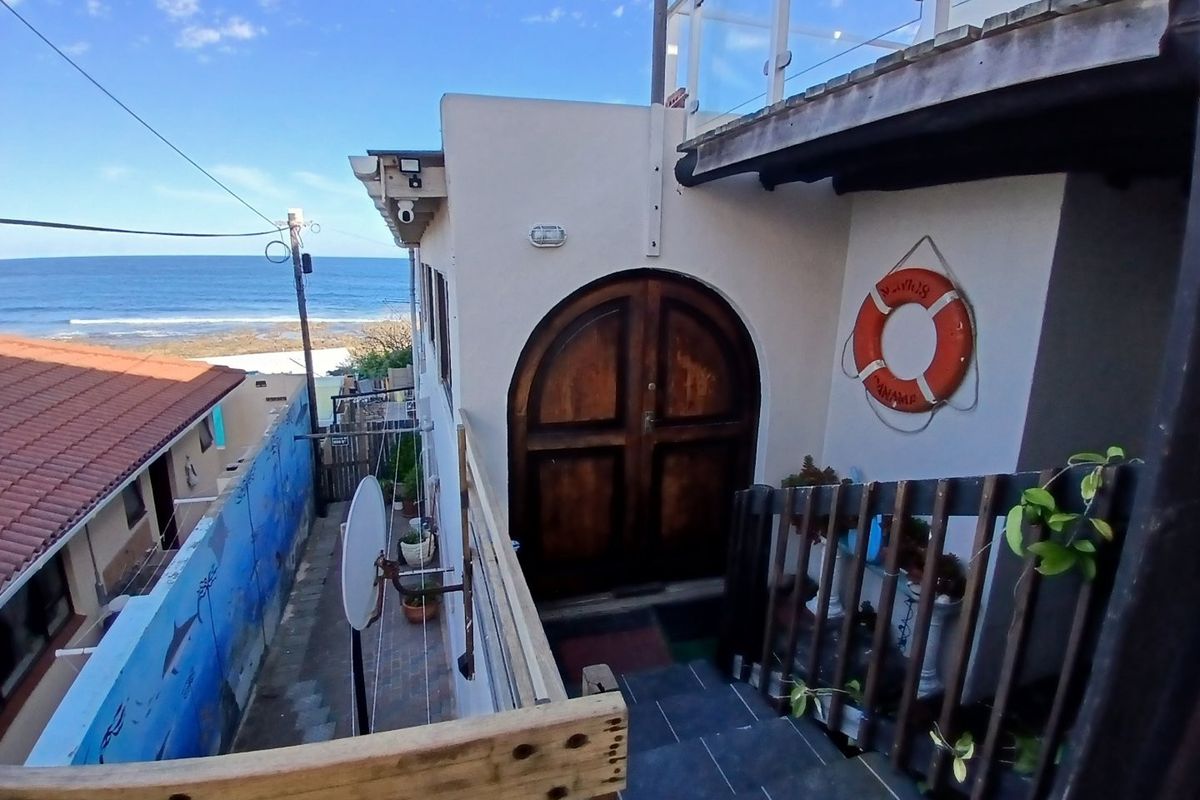 Rear exterior view featuring an arched wooden entrance door, tiled staircase, and glass balustrade with a coastal outlook.