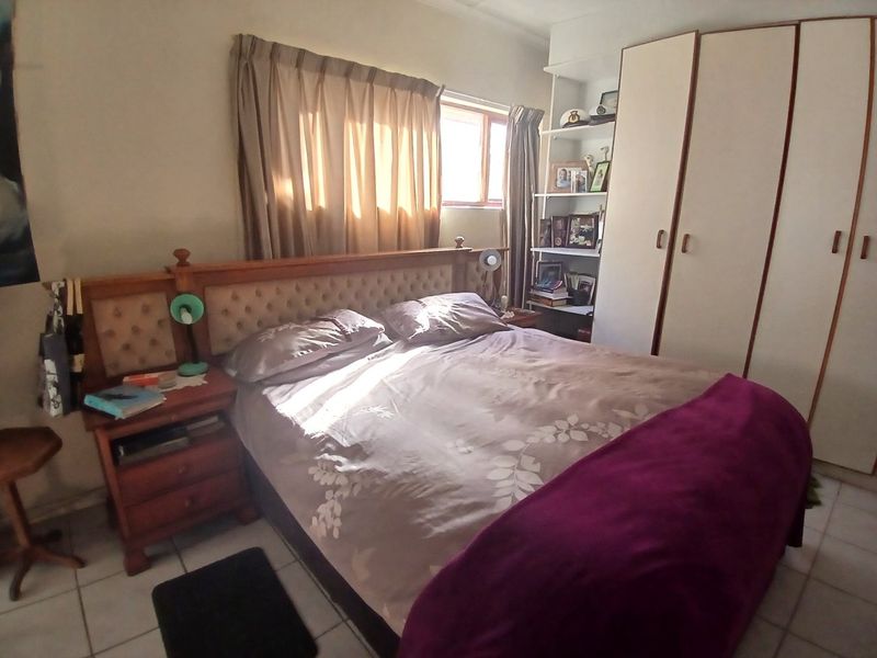 A functional bedroom featuring built-in cupboards, tiled flooring, and integrated shelving, offering a practical layout with natural light.