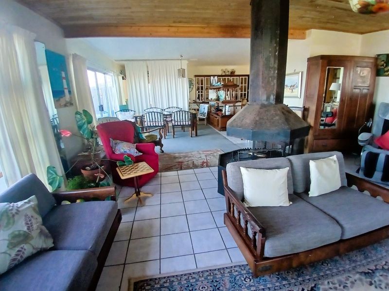 Spacious open-plan living area featuring a central suspended fireplace, tiled flooring, and timber-clad ceilings with access to outdoor space.