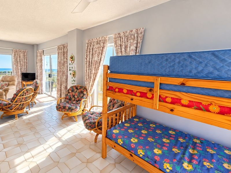 Spacious open-plan living area featuring tiled flooring, ceiling fan, and large sliding glass doors providing access to the balcony and ocean views.