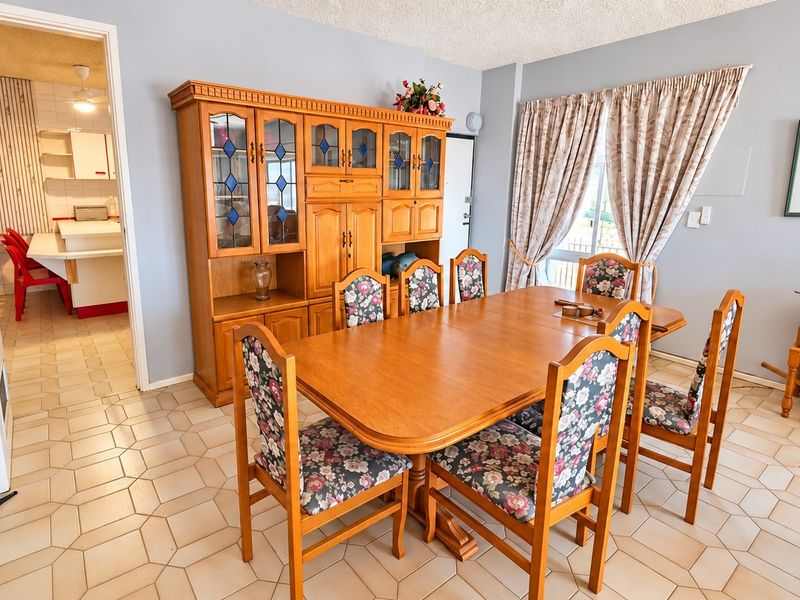 A dining room featuring tiled flooring and a textured ceiling, with an adjacent view into the kitchen area.