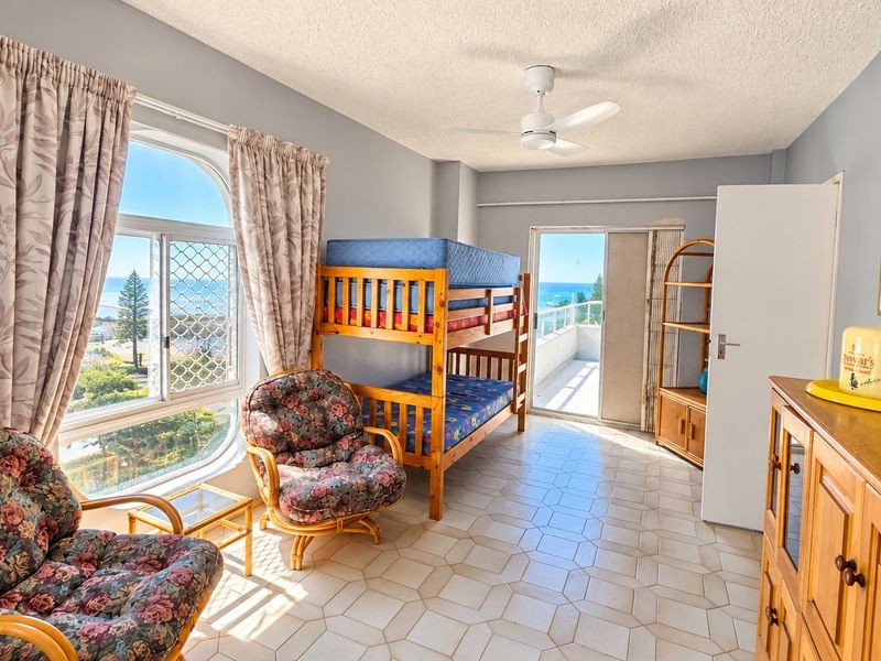 Spacious bedroom featuring tiled flooring, a ceiling fan, and direct access to a private balcony with scenic coastal views.