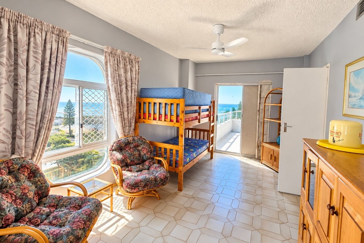 Spacious bedroom featuring tiled flooring, a ceiling fan, and direct access to a private balcony with scenic coastal views.