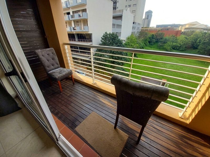 A private balcony featuring timber decking and a metal balustrade, offering an elevated view over the surrounding green space and urban landscape.