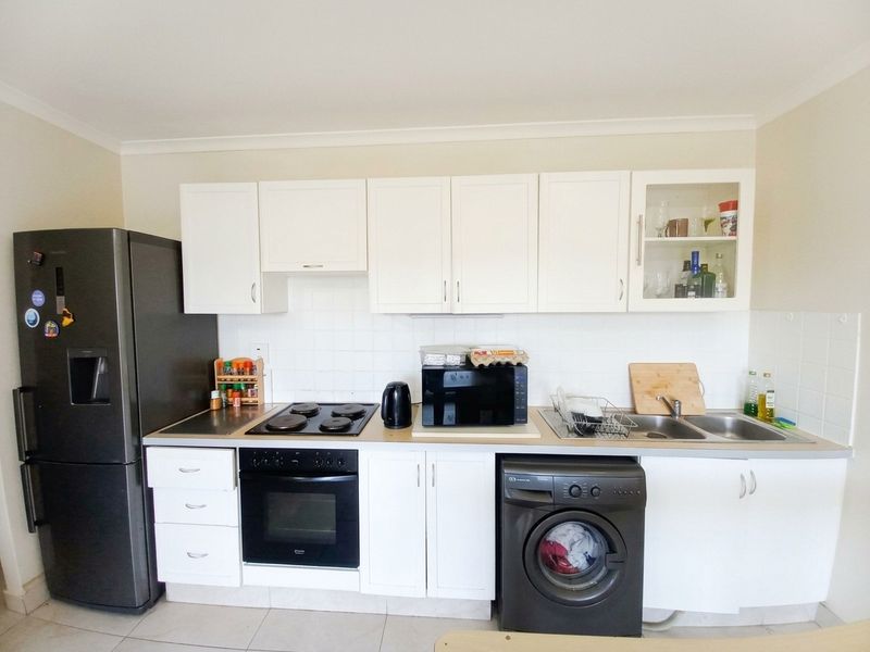 A functional kitchen featuring white cabinetry, a tiled backsplash, built-in oven, electric hob, and a double sink with tiled flooring.