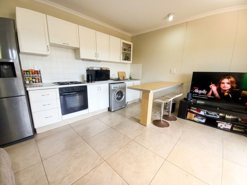 Open-plan kitchen featuring white cabinetry, tiled flooring, built-in oven and hob, and a breakfast bar, seamlessly integrated with the living area.