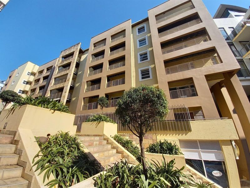 A low-angle view of a multi-story apartment building featuring tiered stone staircases, landscaped planters, and private balconies with metal railings.