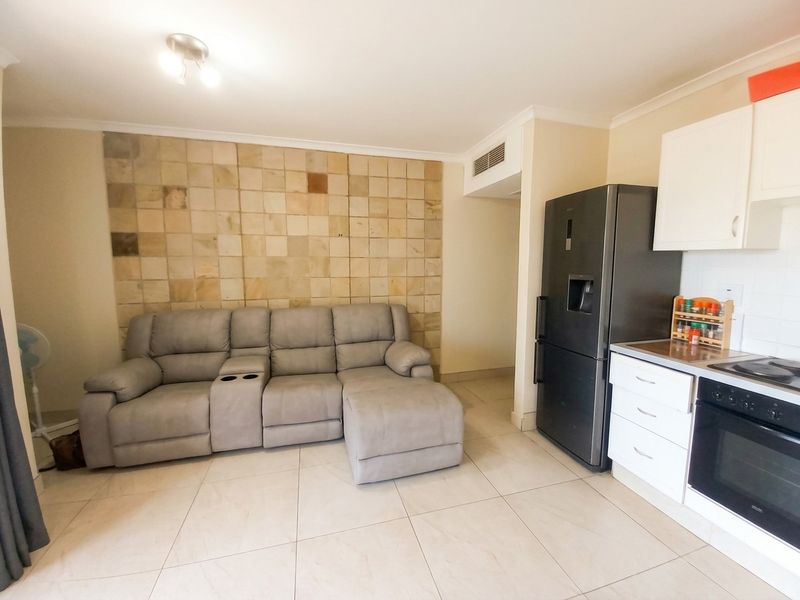 Open-plan living area featuring tiled floors, a stone feature wall, and a compact kitchen with built-in oven and hob.