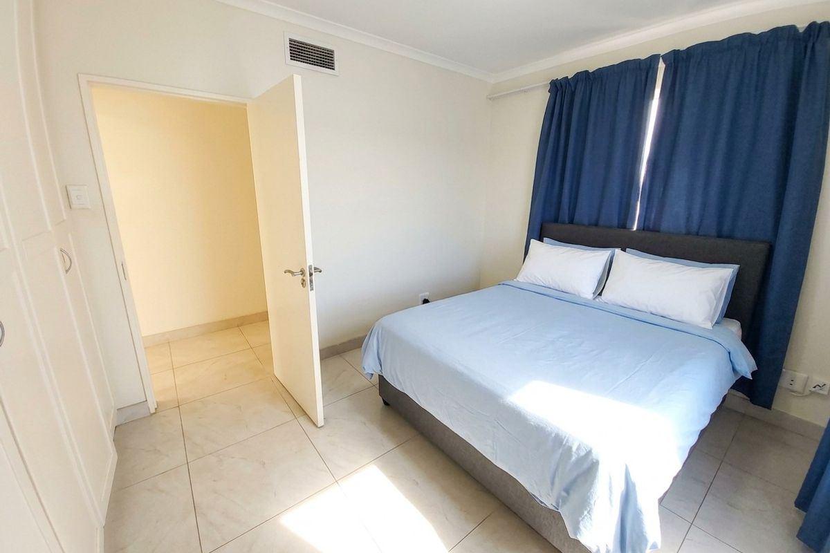A bright bedroom featuring neutral tiled flooring, built-in cupboards, and an integrated air conditioning vent, offering a clean and functional living space.