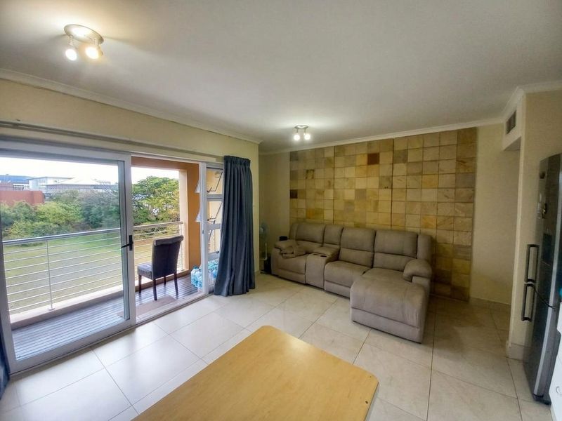 Spacious living room featuring large sliding glass doors leading to a balcony, neutral tiled flooring, and a decorative stone feature wall.