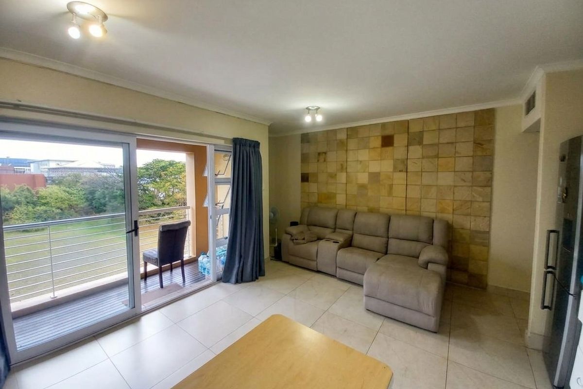 Spacious living room featuring large sliding glass doors leading to a balcony, neutral tiled flooring, and a decorative stone feature wall.