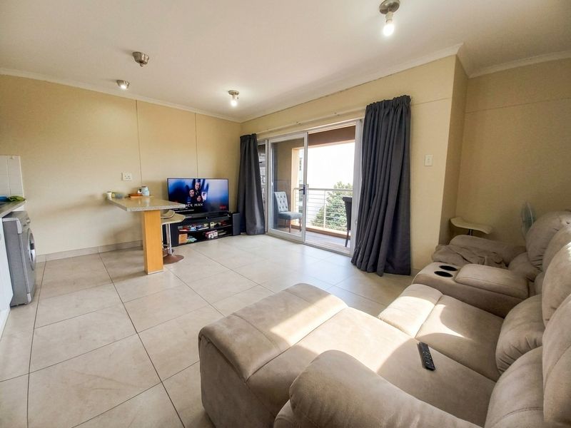 Open-plan living area featuring tiled floors, a breakfast bar, and sliding glass doors leading to a balcony, providing natural light and functional space.