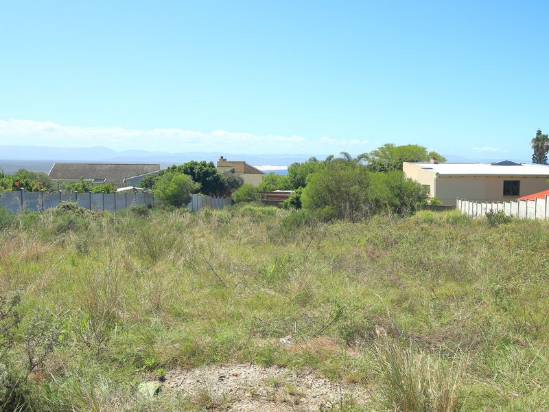 A vacant residential plot featuring natural vegetation and established boundary walls, offering a clear view of the surrounding neighborhood and distant landscape.