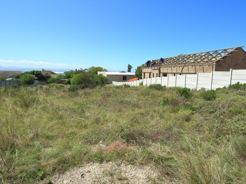 Vacant residential plot featuring natural vegetation, a precast concrete boundary wall, and a structure currently under construction with exposed timber roof trusses.