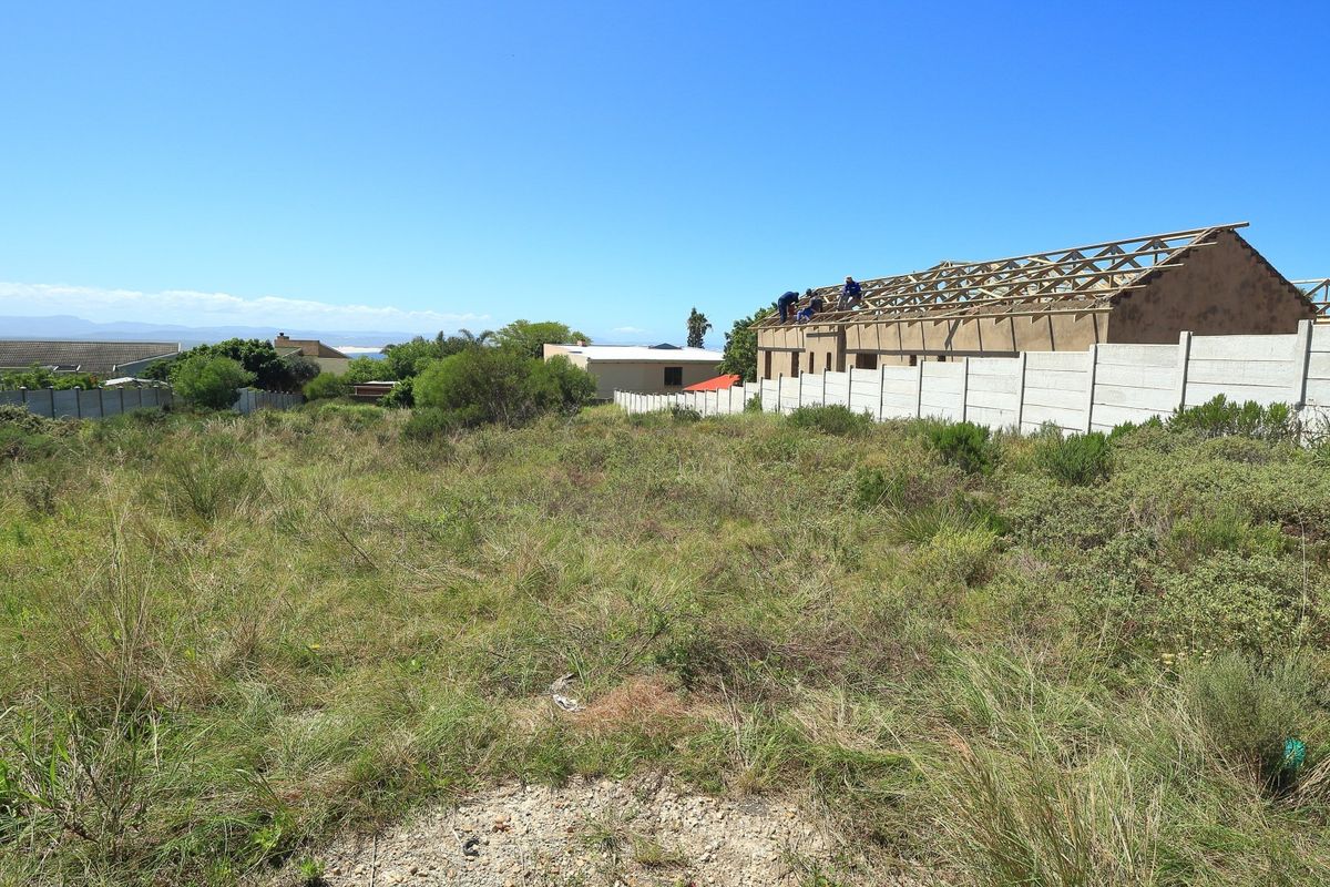 Vacant residential plot featuring natural vegetation, a precast concrete boundary wall, and a structure currently under construction with exposed timber roof trusses.