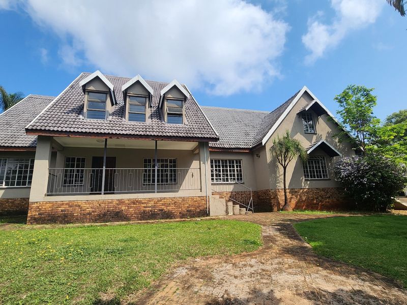 A well-maintained double-story house featuring a tiled roof, dormer windows, brick facade, and a covered front patio with a paved walkway.