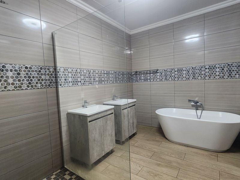 Modern bathroom featuring a freestanding bathtub, dual vanity cabinets, and a glass-enclosed shower area with contemporary tile finishes.
