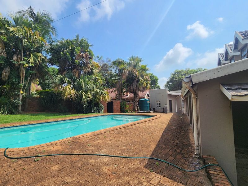 Outdoor pool area featuring a swimming pool, brick paved surround, and established garden landscaping with mature trees.