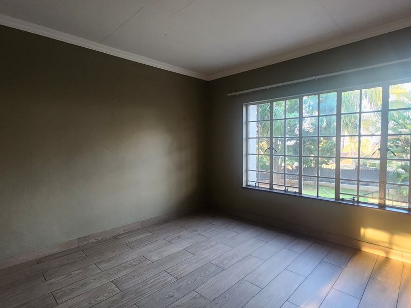 A bright, empty bedroom featuring wood-look tile flooring, neutral wall paint, and a large grid-pattern window providing natural light.
