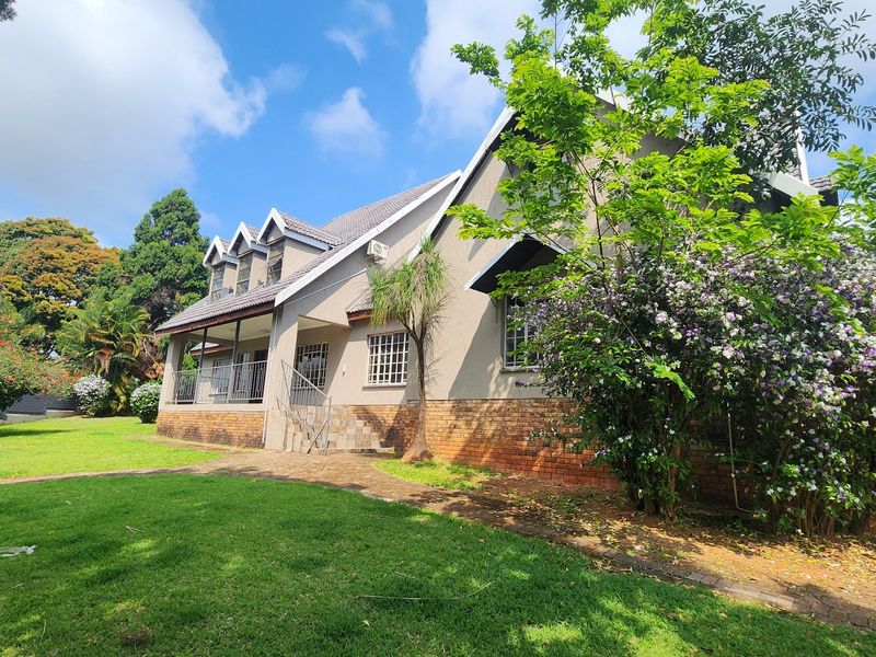 A view of the rear exterior of the house featuring a covered patio, brick and plaster facade, and a well-maintained garden area.
