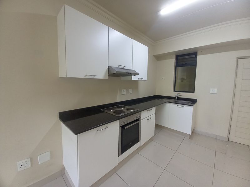 A clean, modern kitchen featuring white cabinetry, dark stone countertops, integrated oven and hob, and tiled flooring in an empty, well-maintained space.