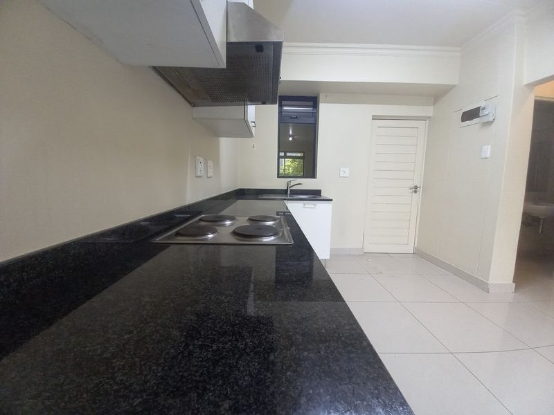 A clean, functional kitchen featuring dark granite countertops, an integrated electric hob, extractor fan, and neutral tiled flooring.