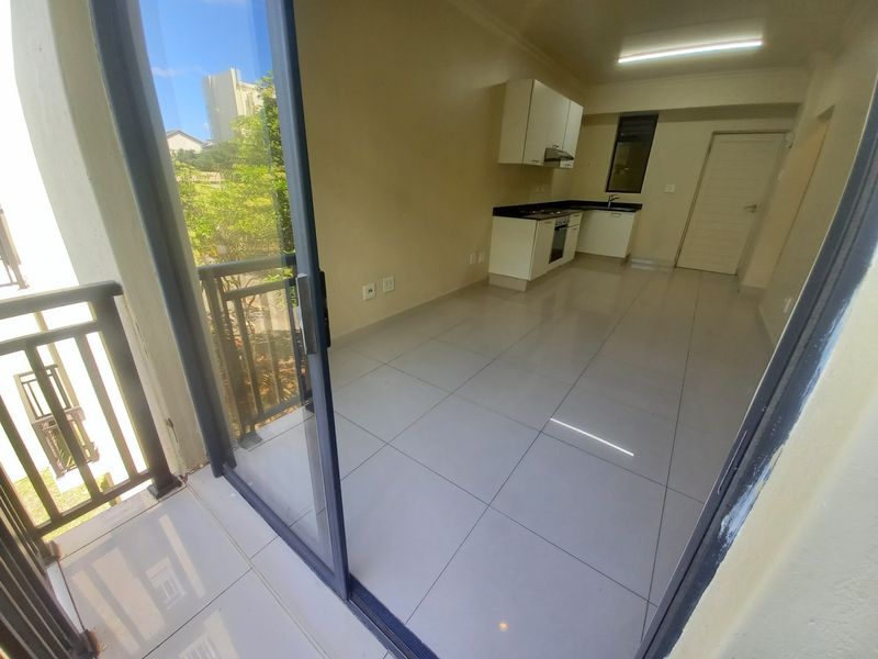 An open-plan living and kitchen area featuring tiled floors, built-in cabinetry with integrated appliances, and direct access to a private balcony.