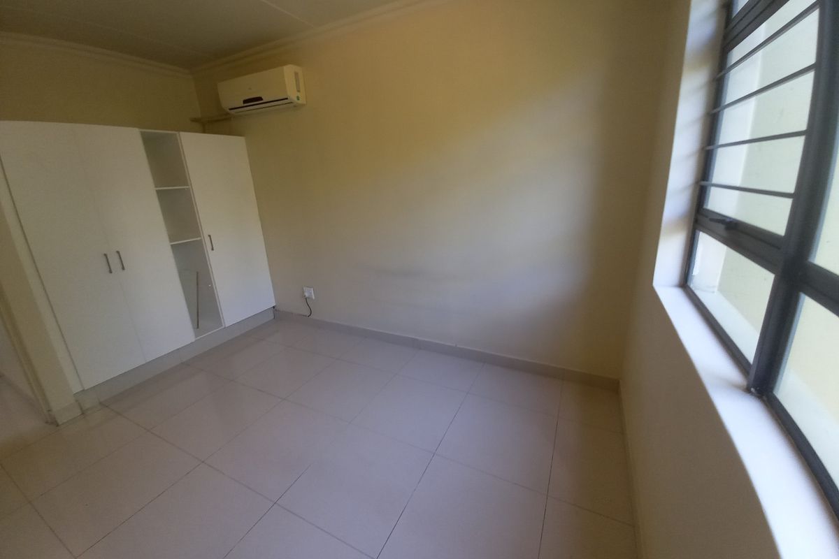 An empty bedroom featuring tiled flooring, built-in cupboards, and a wall-mounted air conditioning unit.