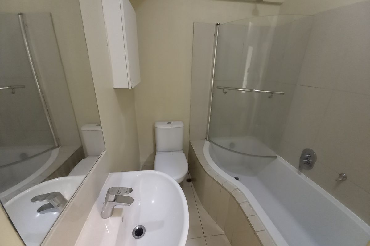 A functional bathroom featuring a curved bathtub with a glass shower screen, a pedestal vanity basin, and a standard toilet.