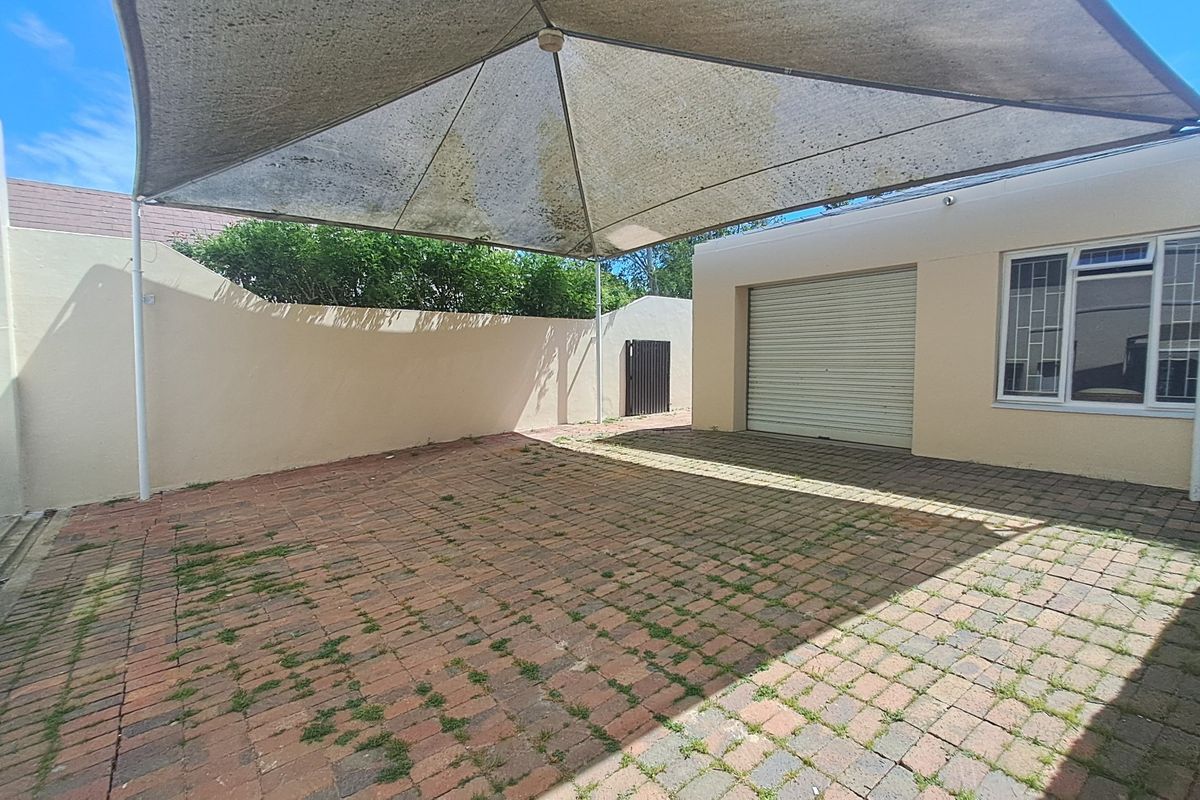 A paved rear courtyard area featuring a large shade sail, roller garage door access, and perimeter boundary walls.
